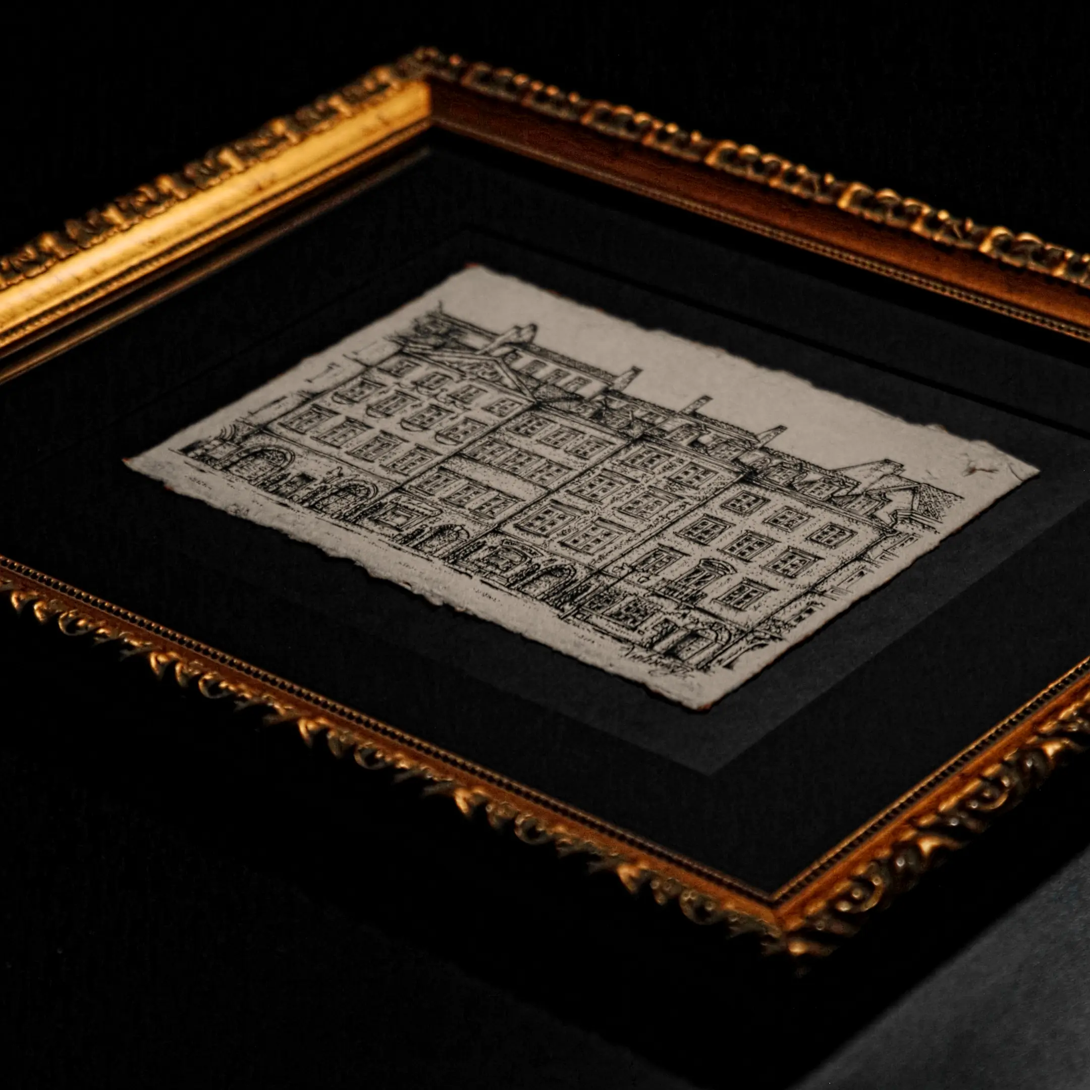 A detailed black ink drawing of a classic European-style row of buildings on handmade paper with deckled edges, mounted in a black mat and a golden ornate frame.