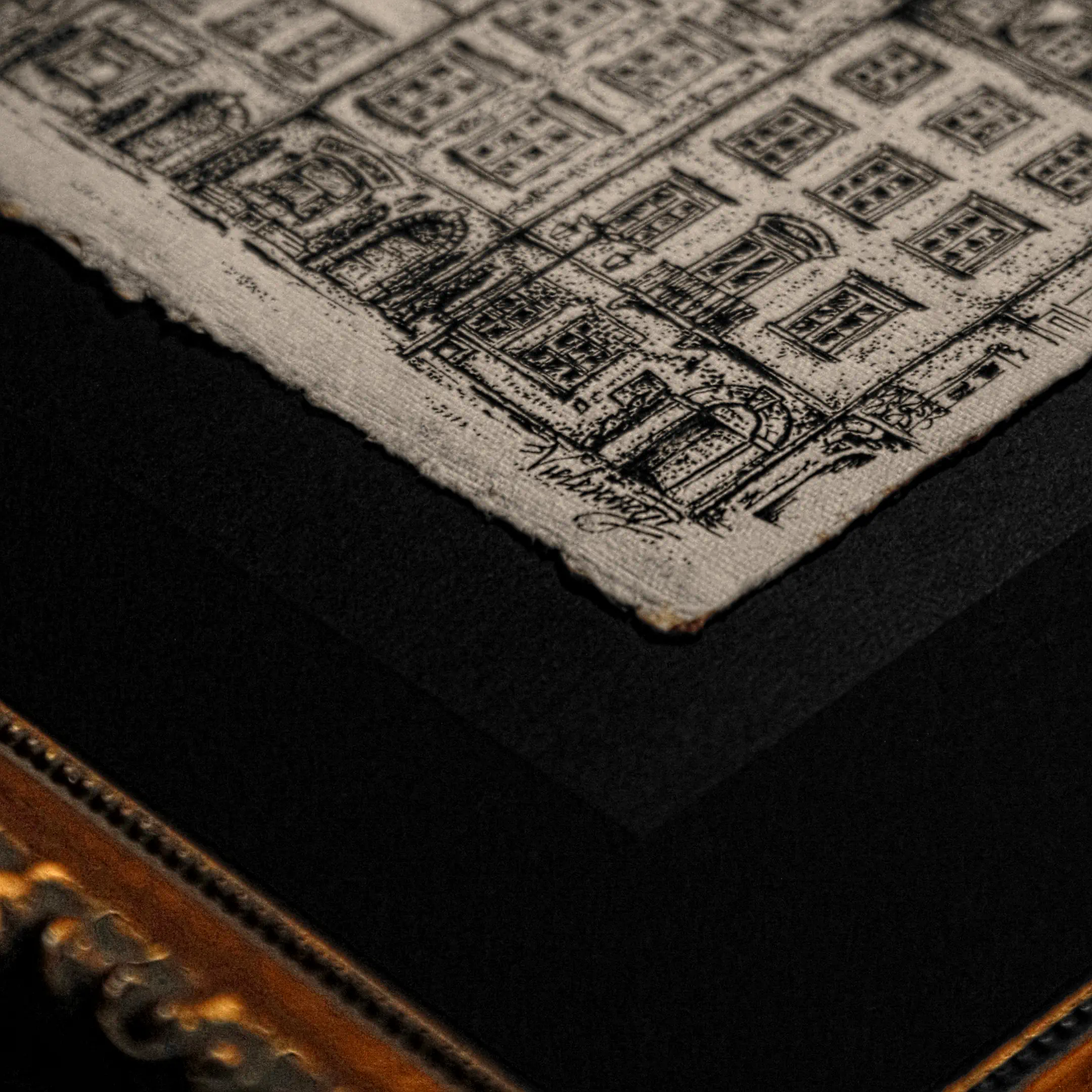 A close-up shot of the bottom corner of an ink drawing on textured paper with deckled edges. Detailed illustrations of building facades are visible along with the clear signature of the artist, Vselenskyi. The piece is set against a black mat and a gold-trimmed frame.