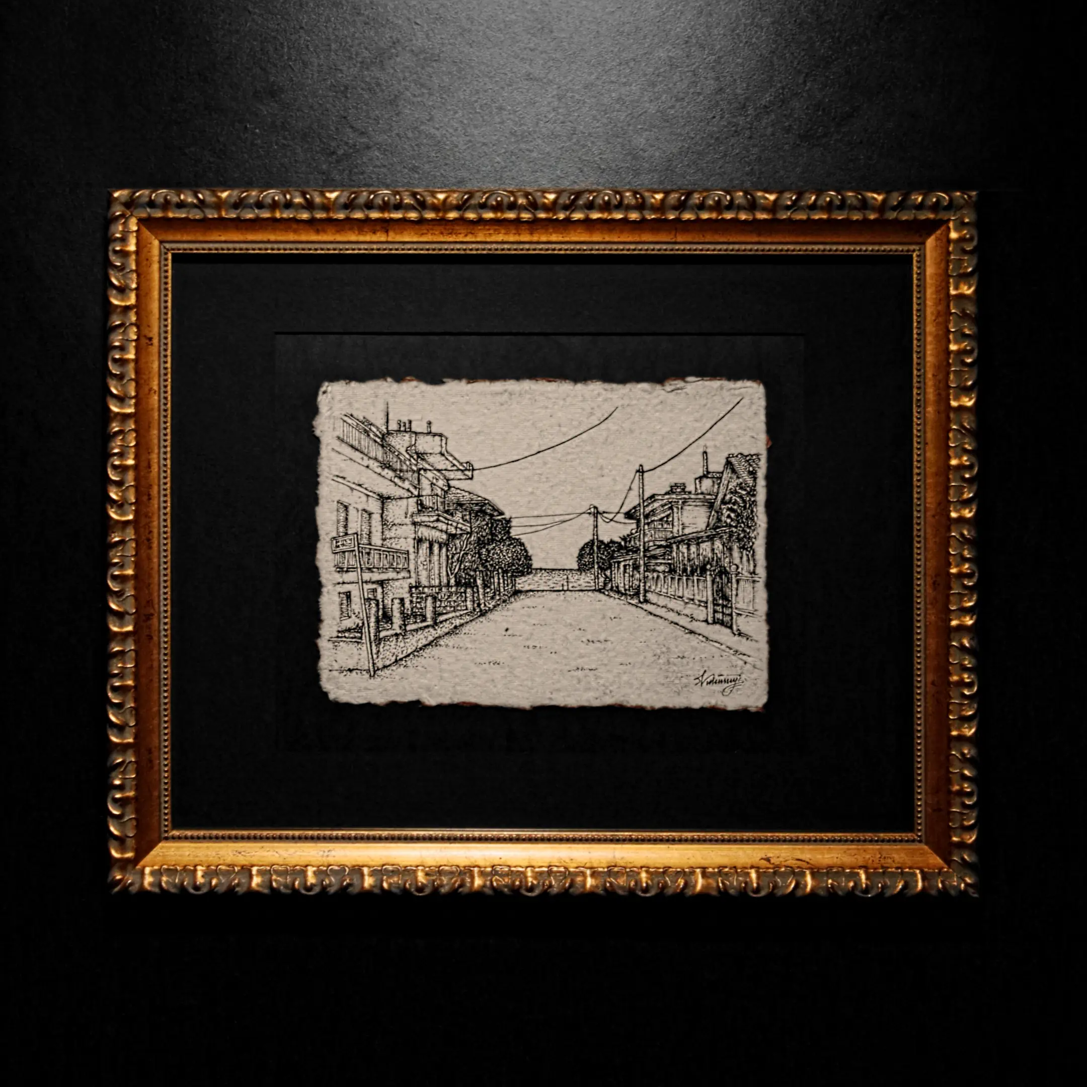 An ink drawing of a city street on deckle-edged paper, matted in black and framed in a classic gold ornate frame against a dark wall.