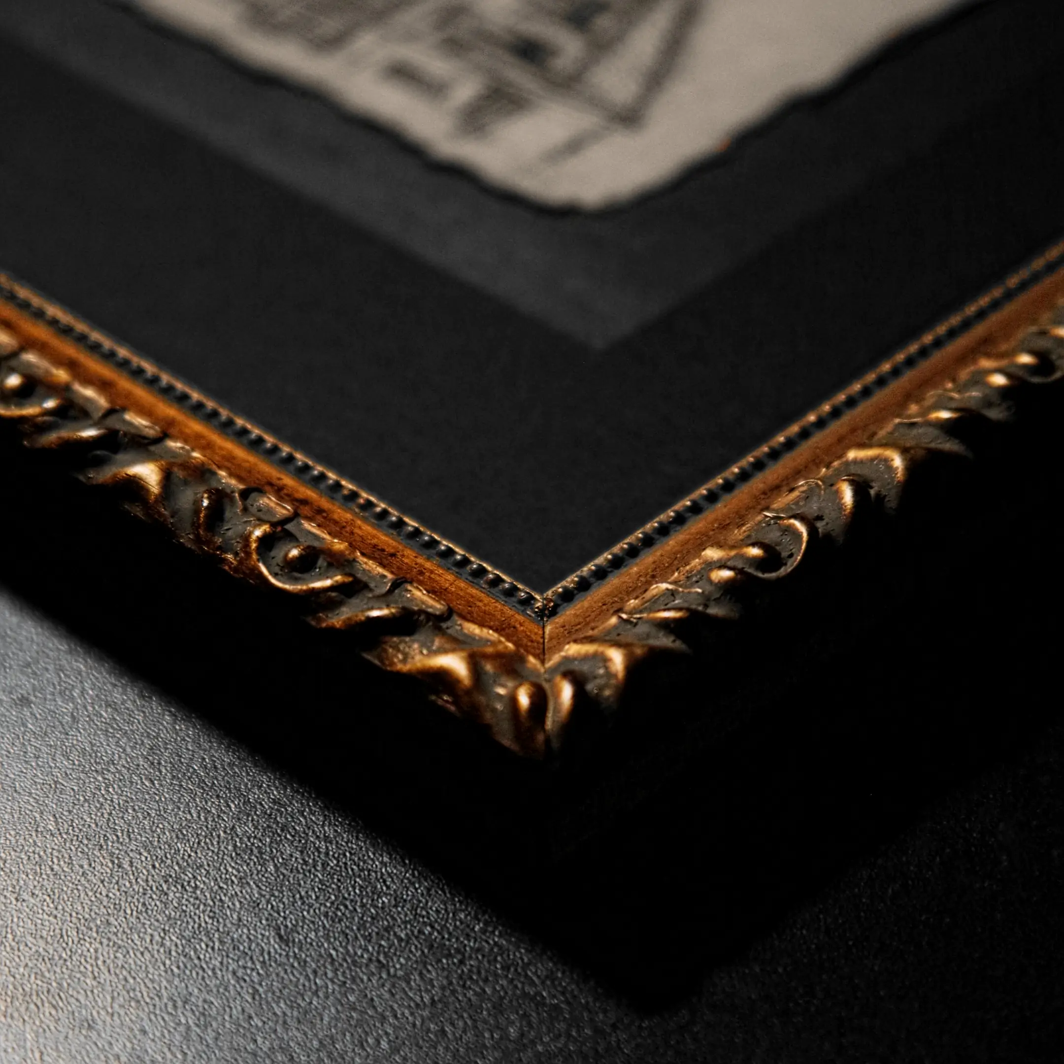 Close-up of a decorative gilded frame corner with a black mat, framing an ink drawing on textured paper.
