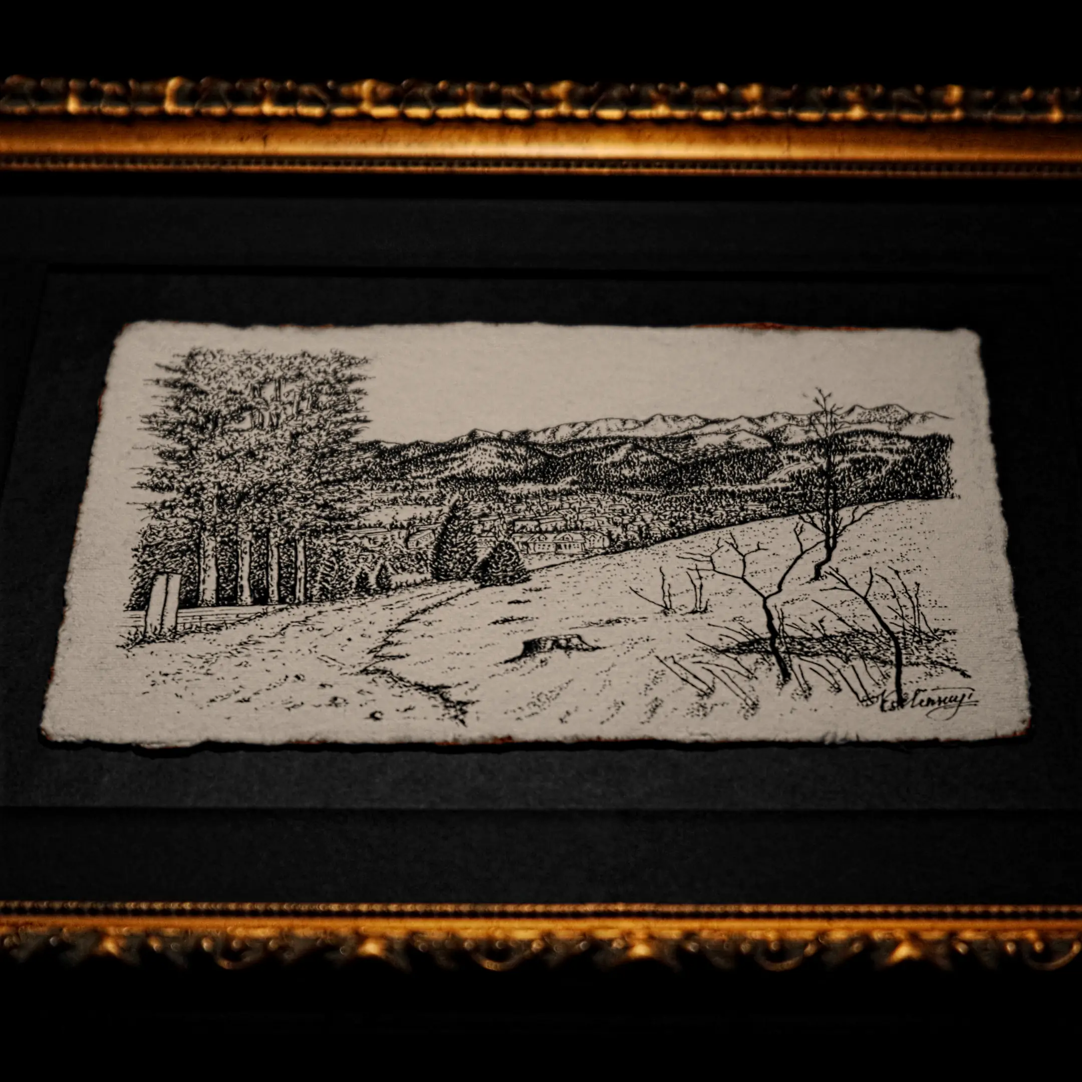 A horizontal ink drawing of a mountain landscape on deckle-edged paper, set within a black mat and a classic gilded gold frame.