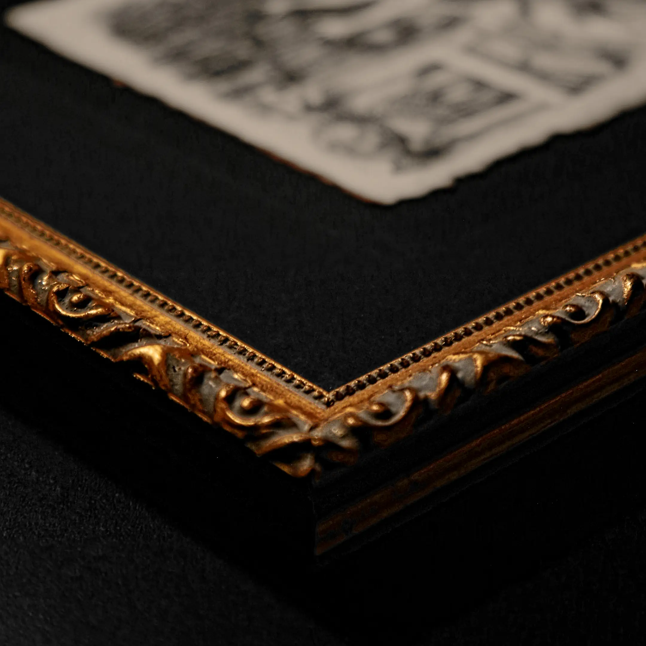 A close-up of the corner of a massive gilded frame with a classical carved pattern. Inside the frame, a black matte pass-partout is visible, holding a fragment of a VSELÉNSKYI® graphic work on thick paper with a deckled edge. Focus on the texture of the molding and the patina.