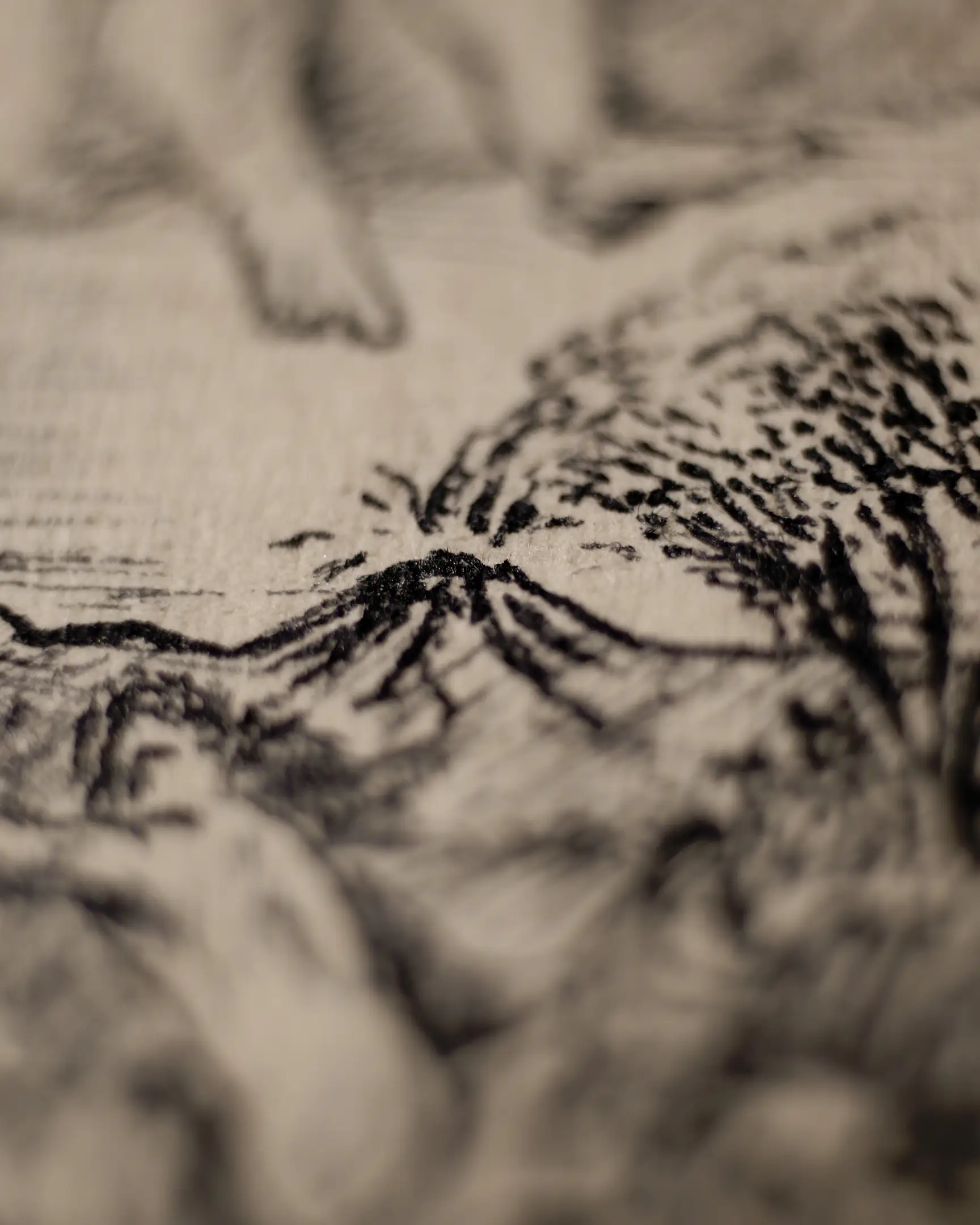 This close-up captures the moment of a volcanic eruption. Dark, dense ink strokes and stippling emerge from the jagged crater of the mountain, representing smoke, ash, and volcanic material being cast into the air. Beside the volcano, a tree with heavy foliage is visible, its form created by a mass of fine dots. The shallow focus emphasizes the raw energy of the eruption against the textured grain of the paper.