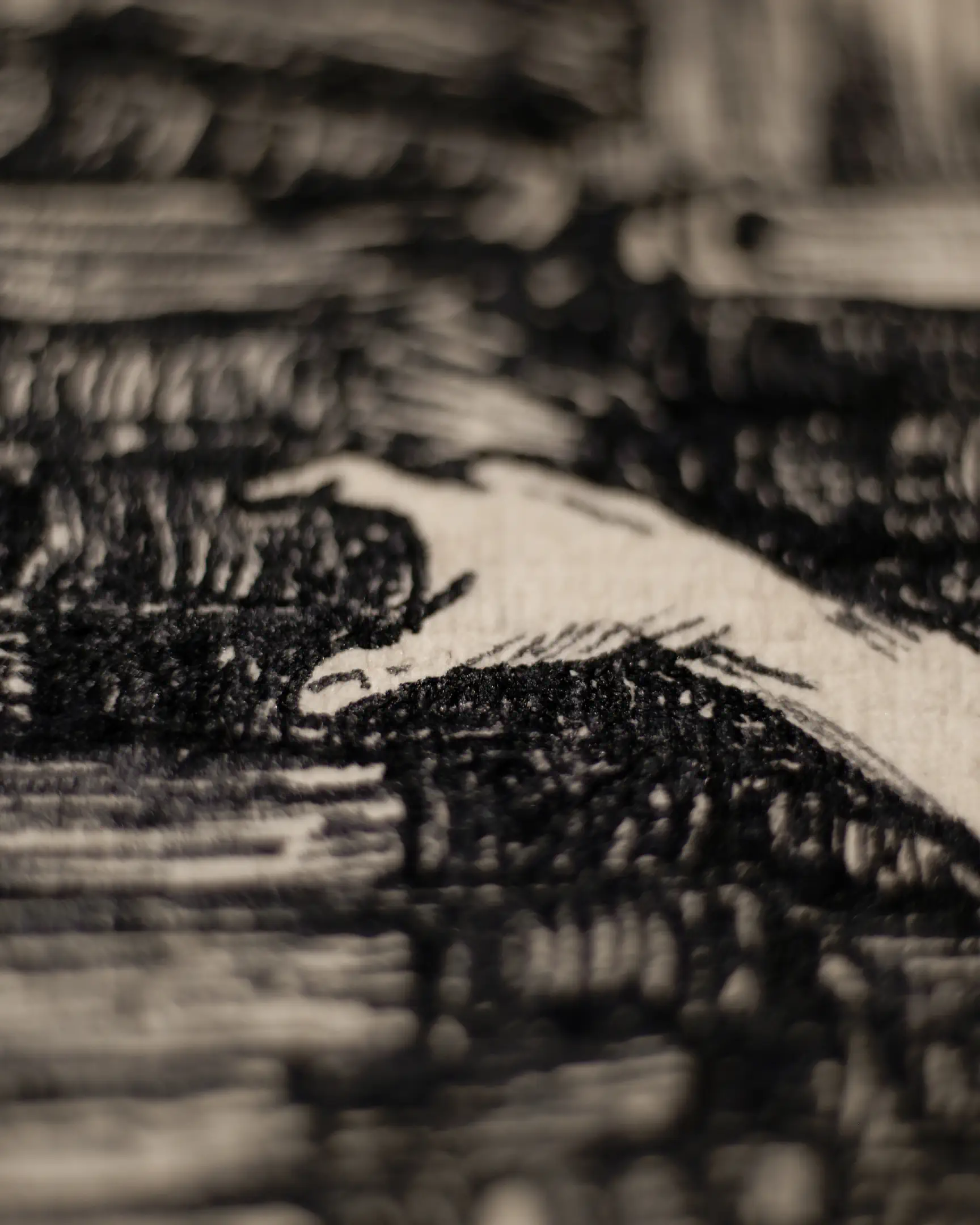 This shot captures a pale hand with extended fingers reaching toward a very dark, heavily hatched area. The contrast between the blank paper of the hand and the deep black ink around it creates a sense of tension. The shallow depth of field keeps the focus on the hand, while the surrounding background consists of blurred, horizontal and diagonal ink strokes on textured paper.