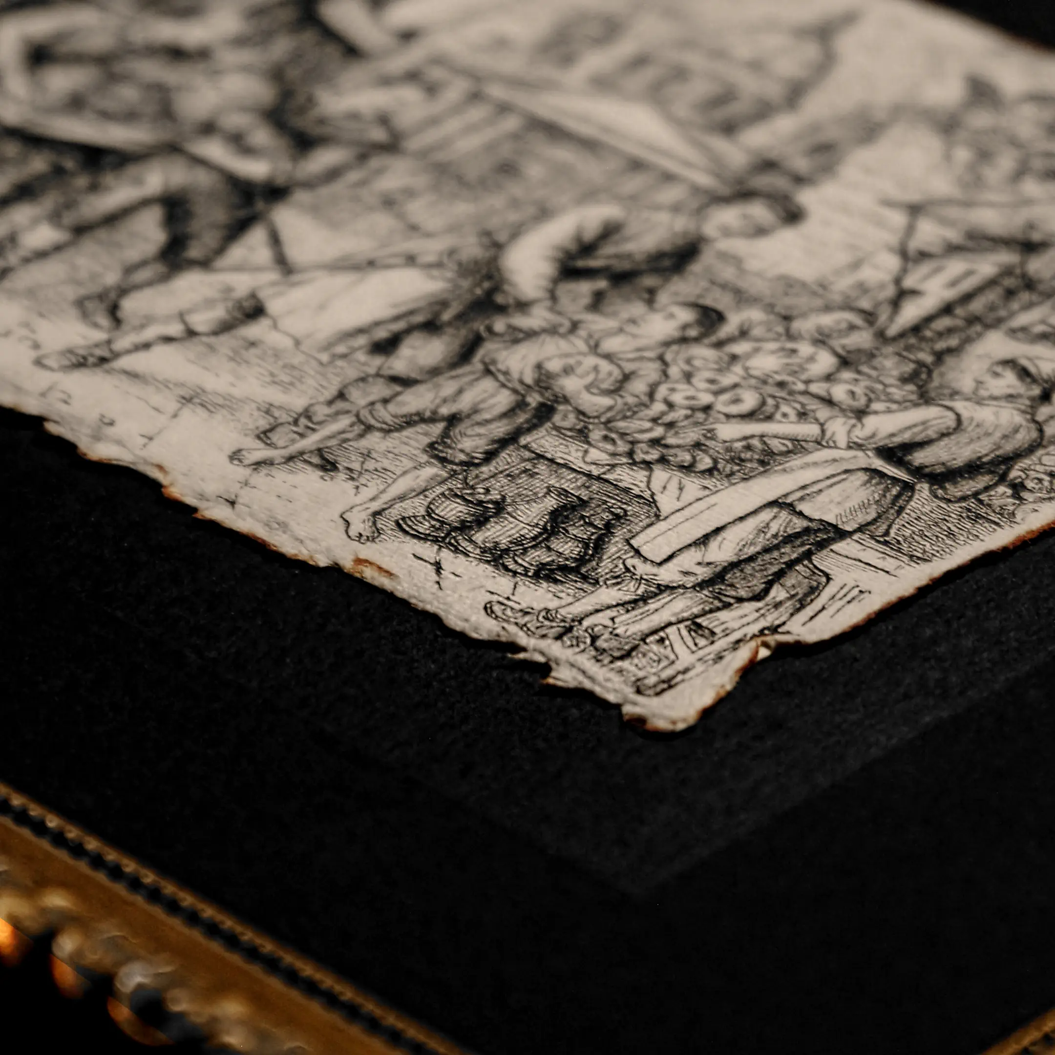 A shallow depth-of-field macro shot focusing on the deckled edge of a thick, off-white paper with an ink drawing, resting on a textured black mat.