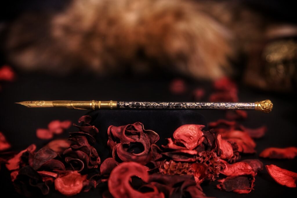 Antique handcrafted pen with intricate patterns resting on a bed of dried red rose petals.