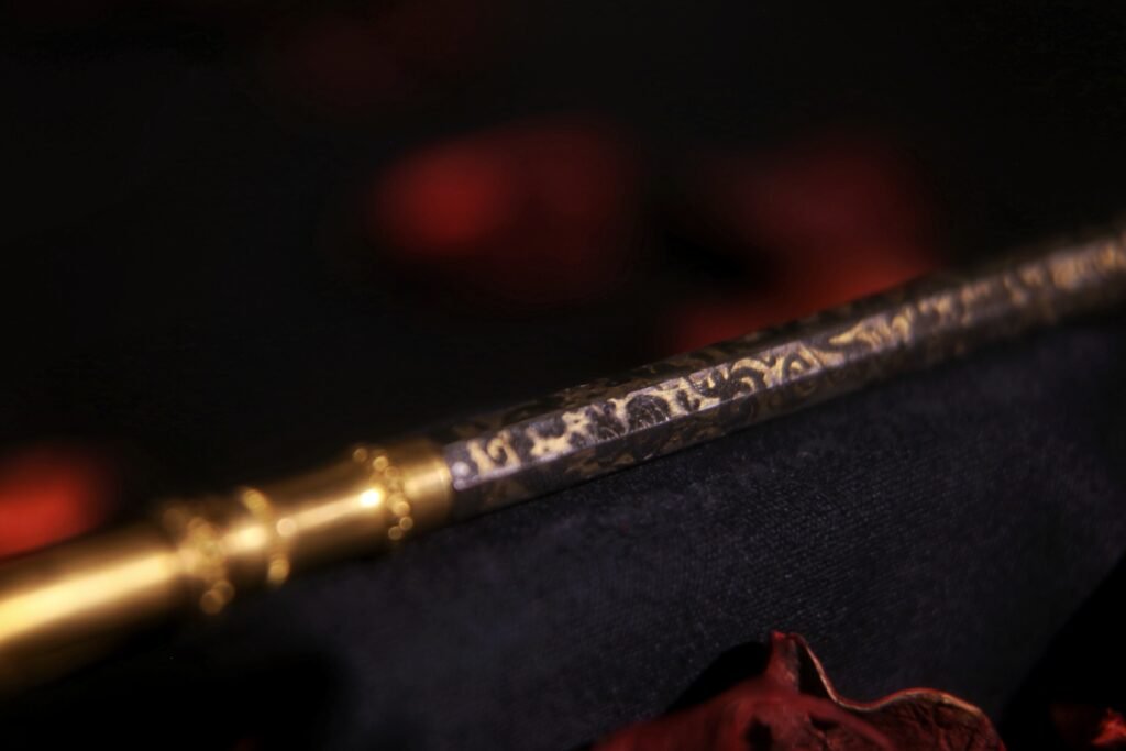 Macro detail of an antique ink dip pen featuring intricate gold and engraved ornate patterns.